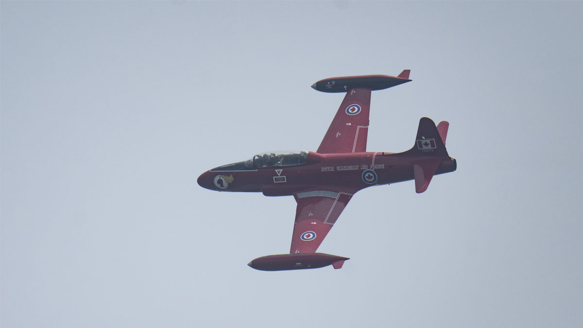 Red military jet flying against a cloudy sky.