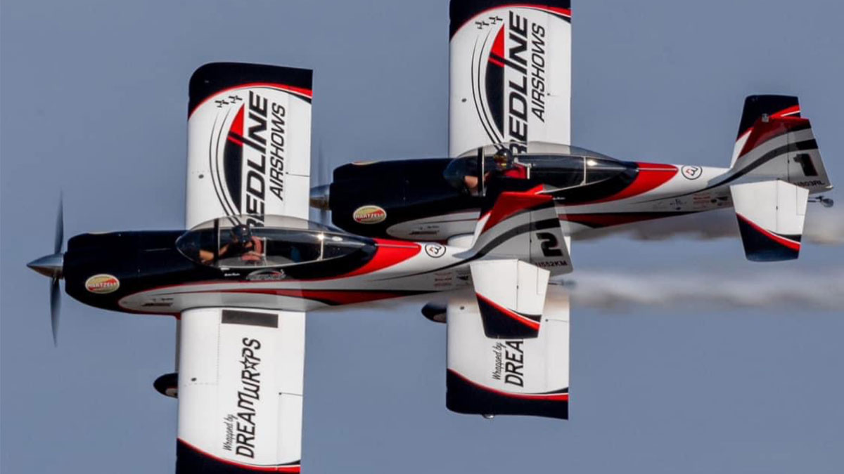 Two stunt airplanes performing acrobatics in a clear blue sky.