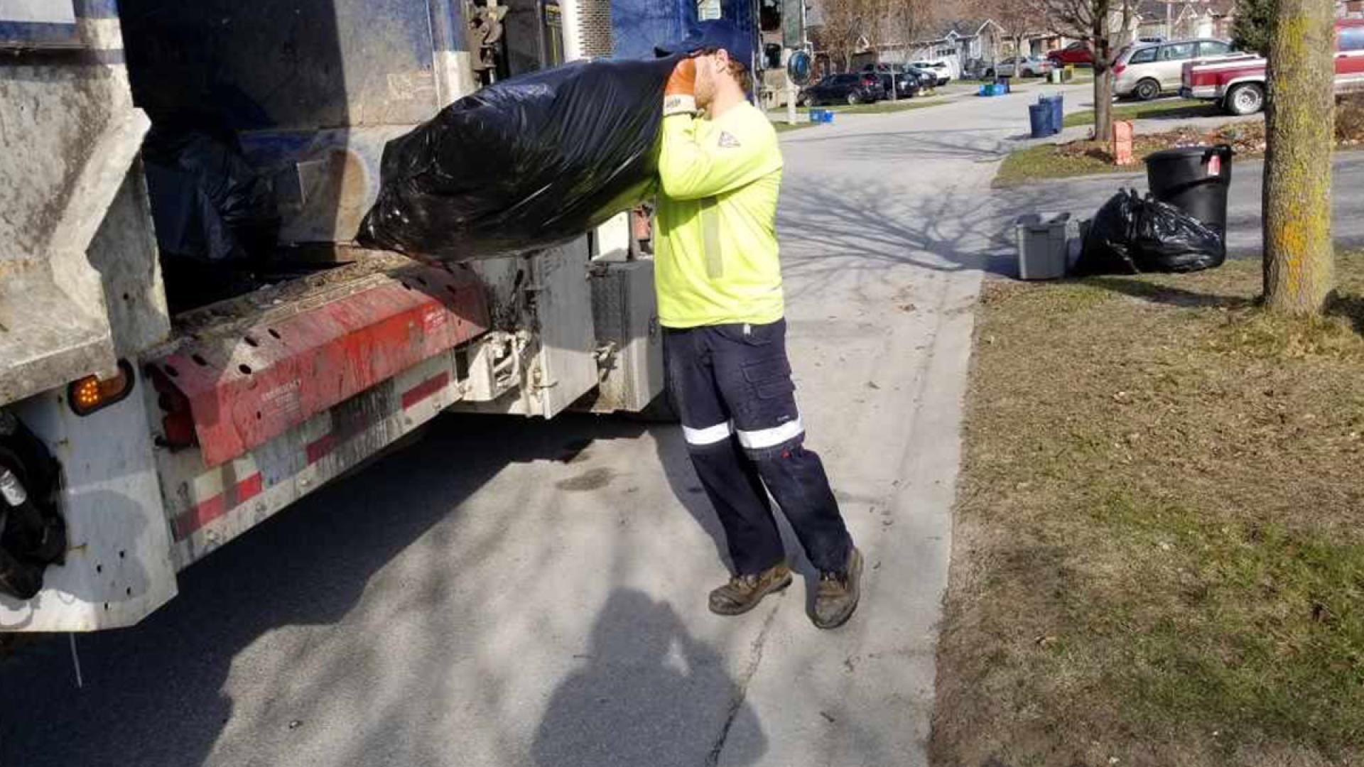 Collector placing garbage bag in collection truck