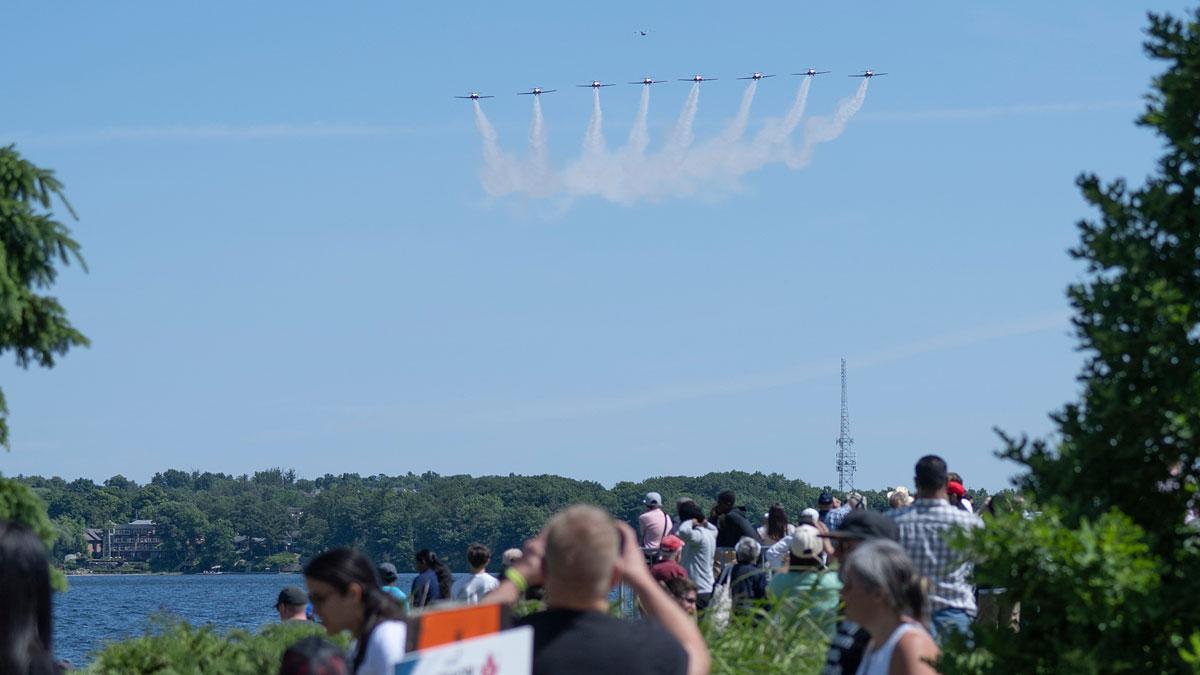 Crowd watches a flight formation of eight planes against a clear blue sky.