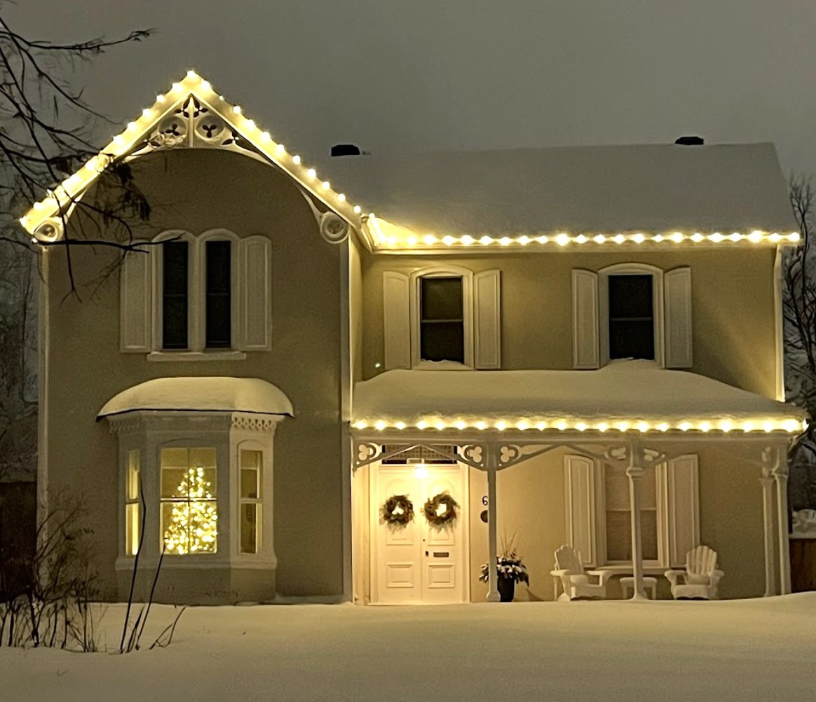 Two-story house with Christmas lights and snowy lawn at night.
