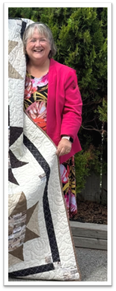 Smiling person holding a large patterned quilt.