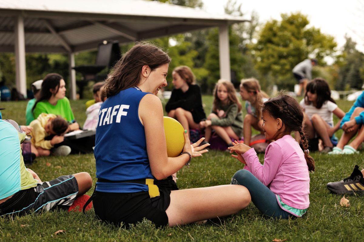 Staff member and children chatting and playing on grass.