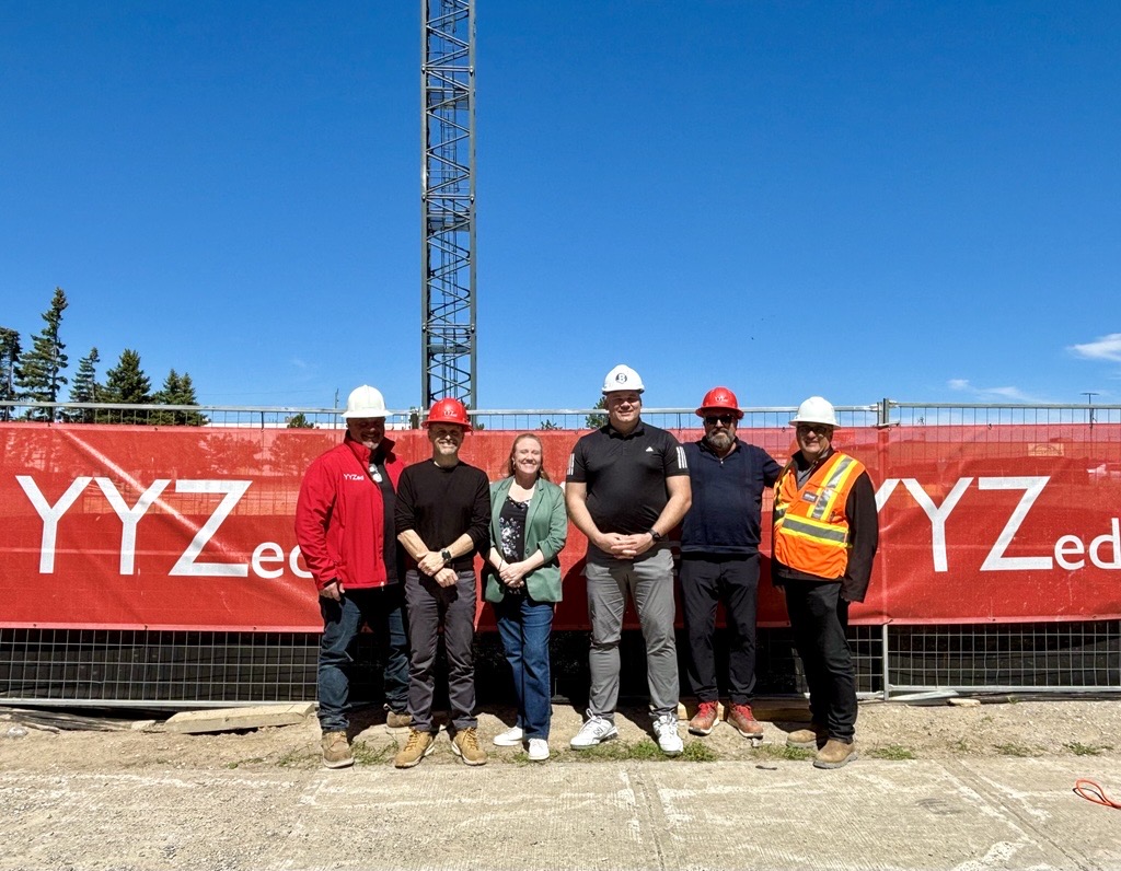 Group of people in construction helmets posing in front of a worksite.
