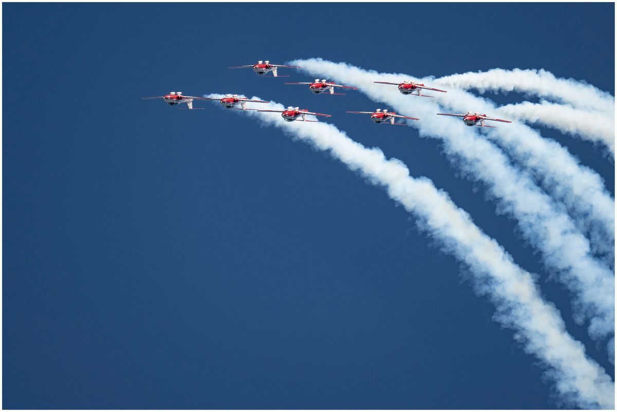 Eight red jets trail white smoke in a blue sky during a synchronized aerial display.