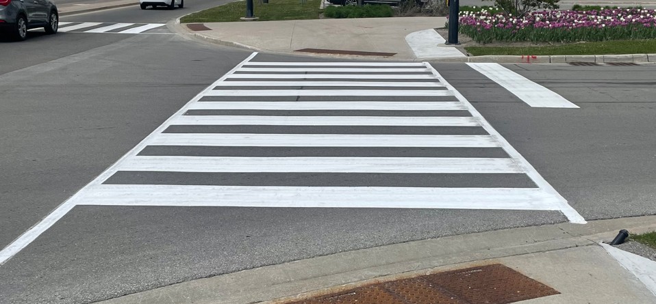 Wide crosswalk with prominently marked white stripes, located at an intersection.