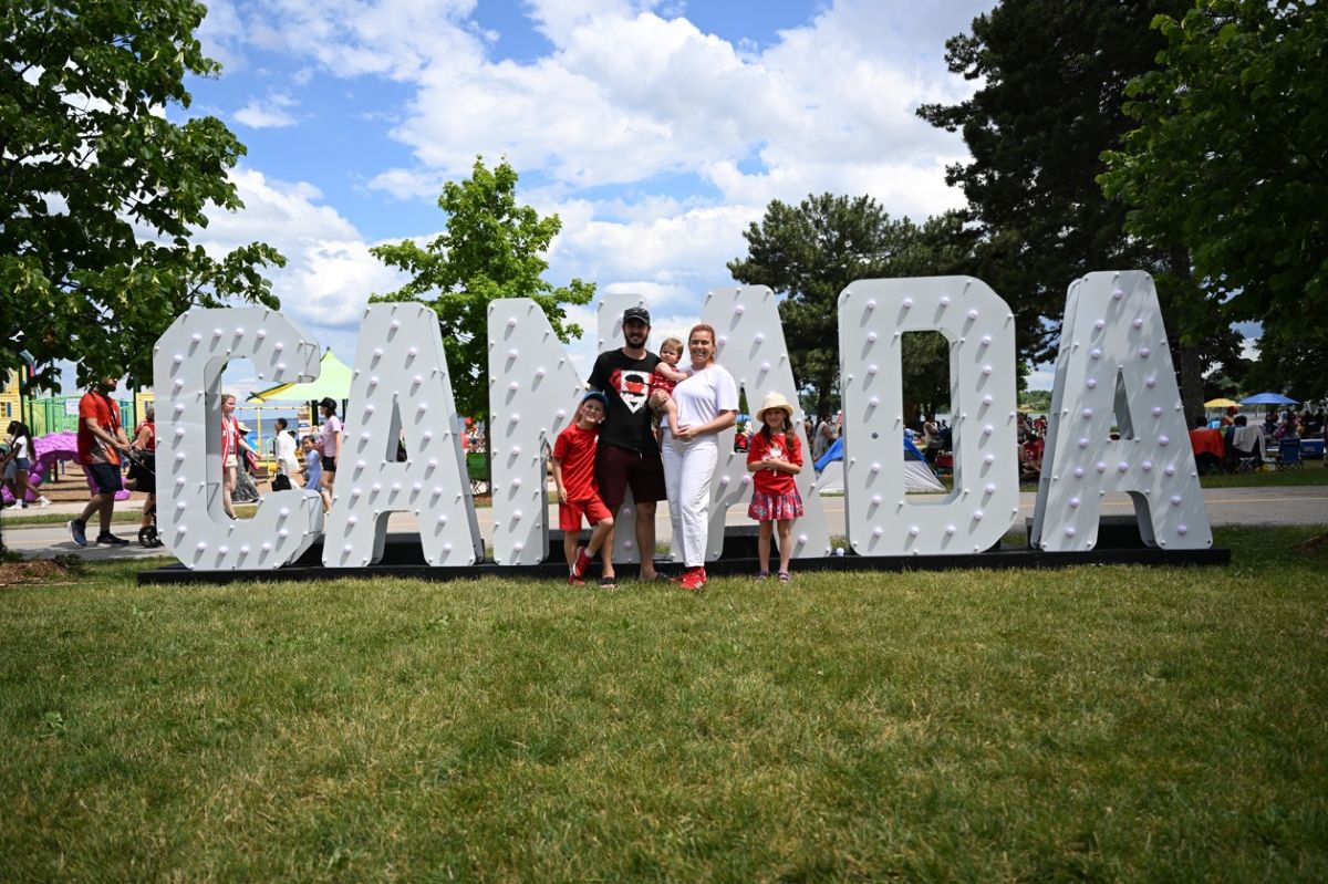 A group of five people in front of large, illuminated letters spelling "CANADA" on a grassy area.