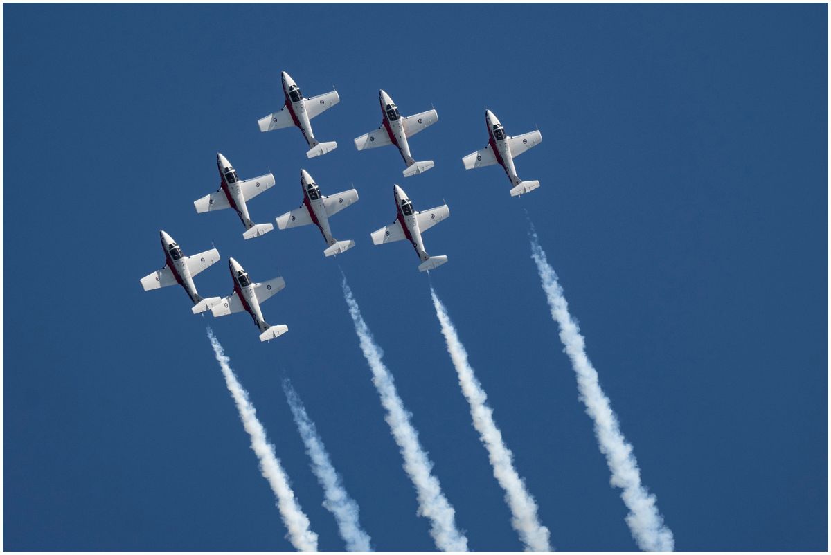 Eight military planes flying in formation, leaving white vapor trails in a blue sky.