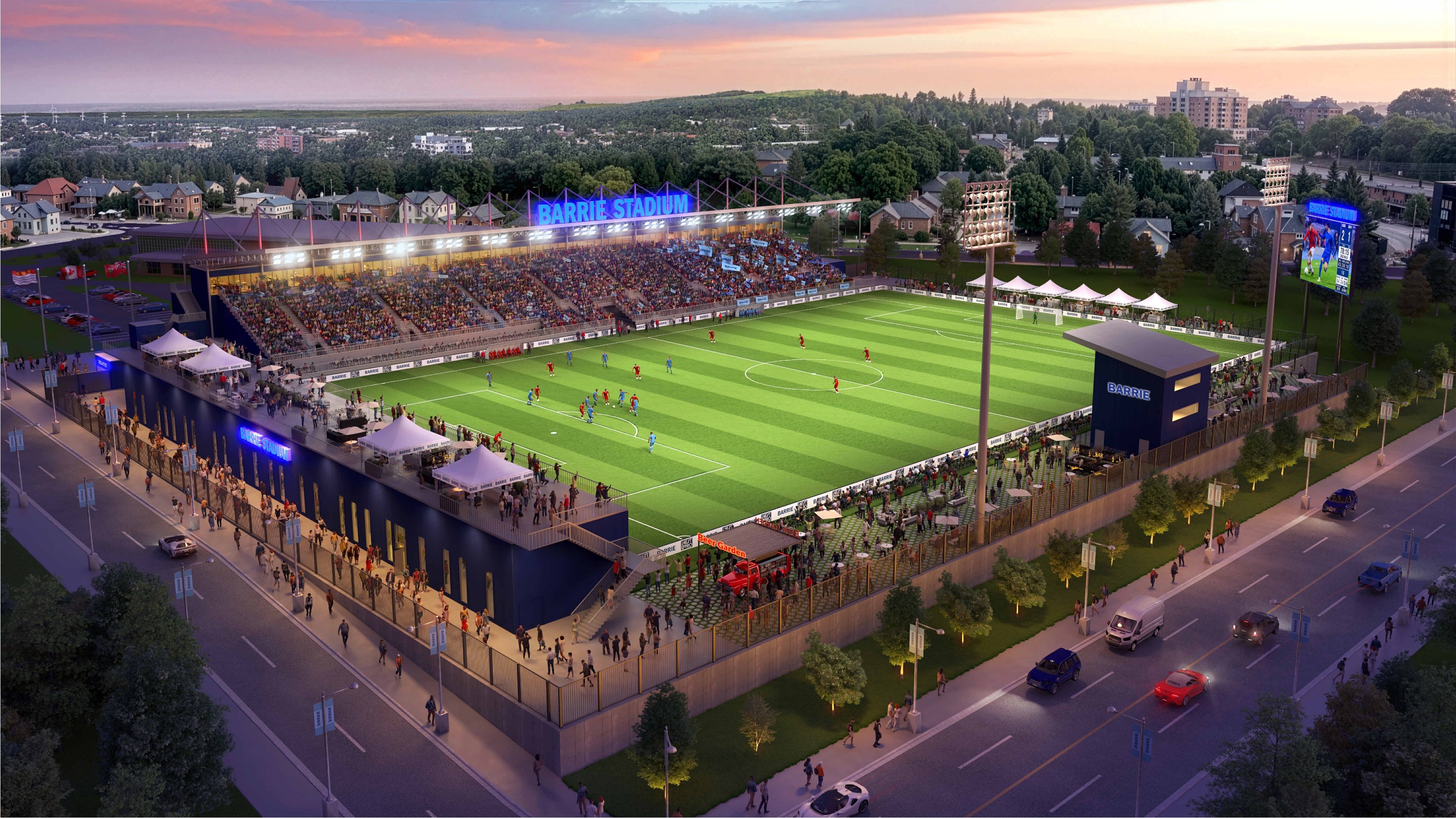 Aerial view of a soccer stadium with green field, seating, and surrounding urban landscape at sunset.
