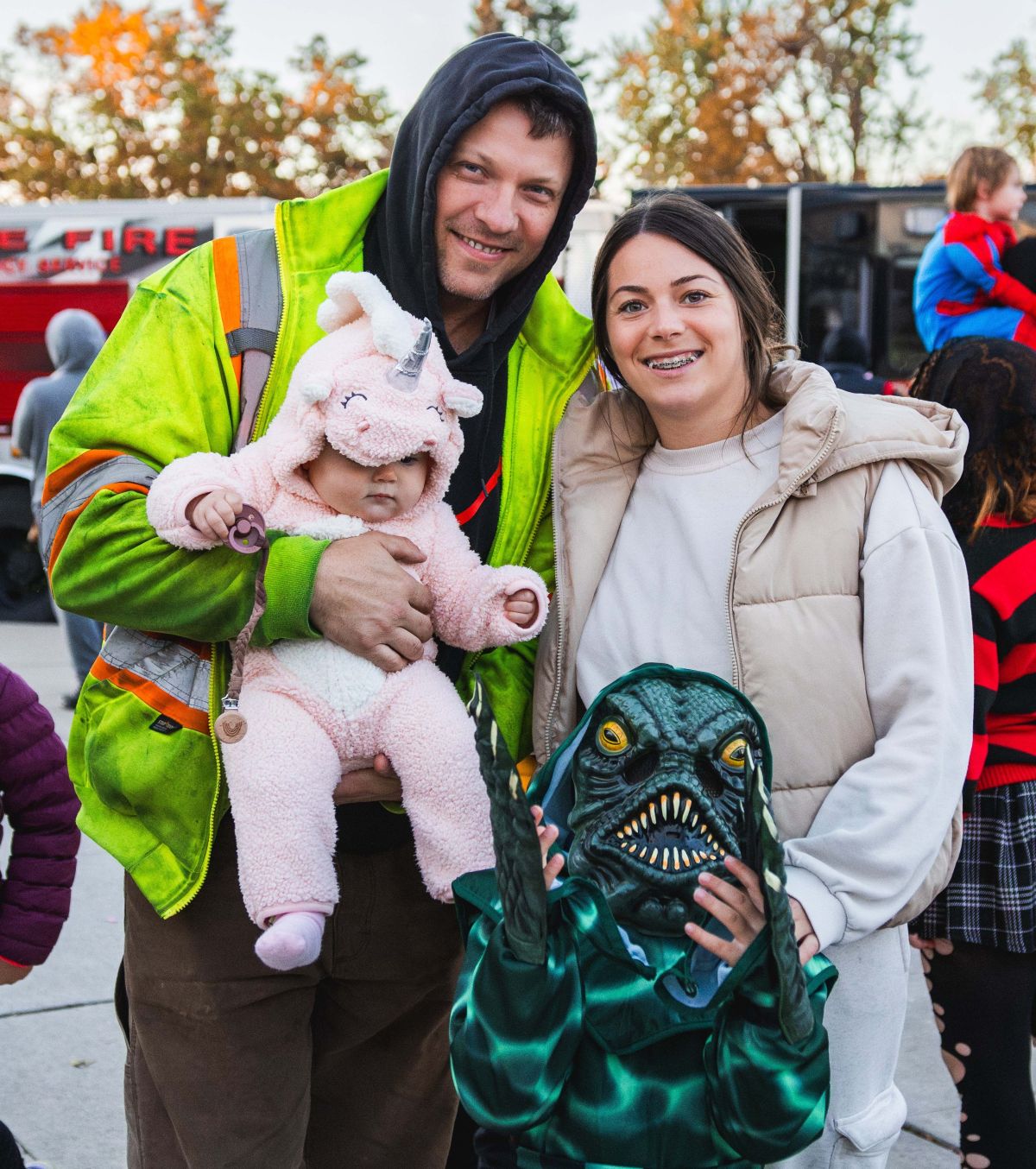 A family including smiling parents, a baby in a unicorn costume and a child in a reptilian costume.