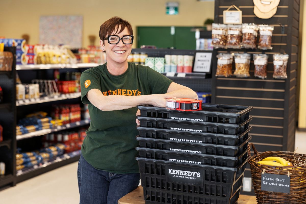 Smiling staff person standing by "Kennedy's Lakeside Grocery" grocery baskets in a store aisle.