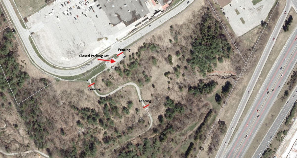 Aerial view of a wooded area with winding paths, parking lot with an arrow noting closed, and nearby road.