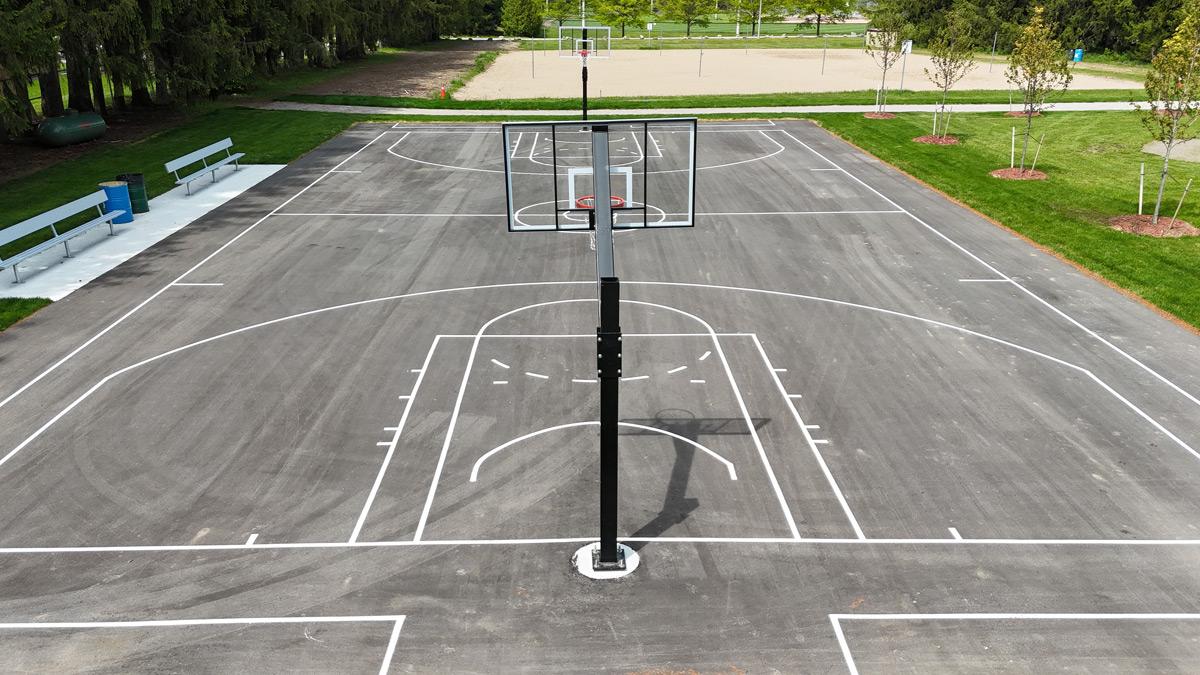 Outdoor multi-use court with basketball nets, with trees and park areas visible in the background.