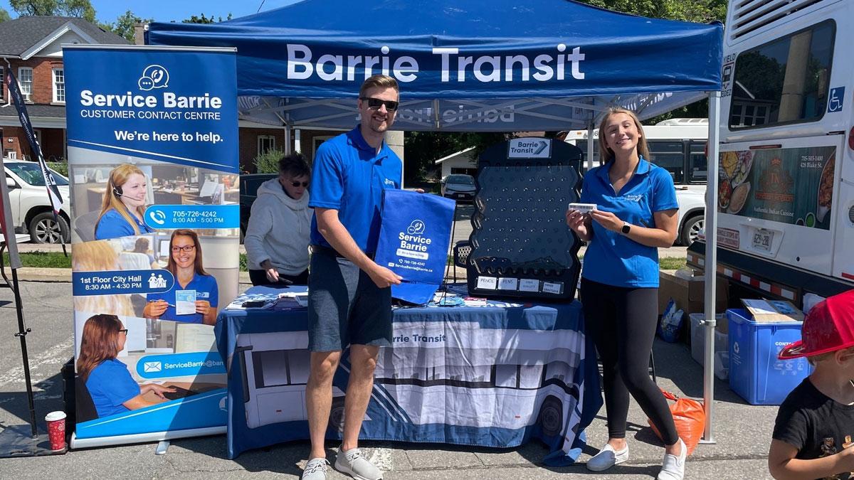 Staff smiling in front of outdoor booth near Service Barrie banner and Barrie Transit tent