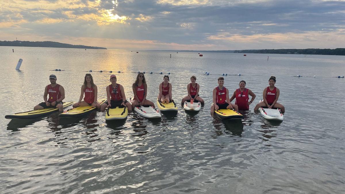 9 lifeguards floating on boards in lake, sunrise in background