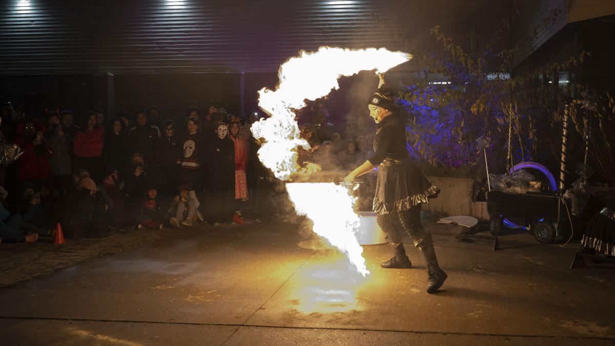 A performer is breathing fire during a night-time outdoor event, captivating an audience that is watching intently.