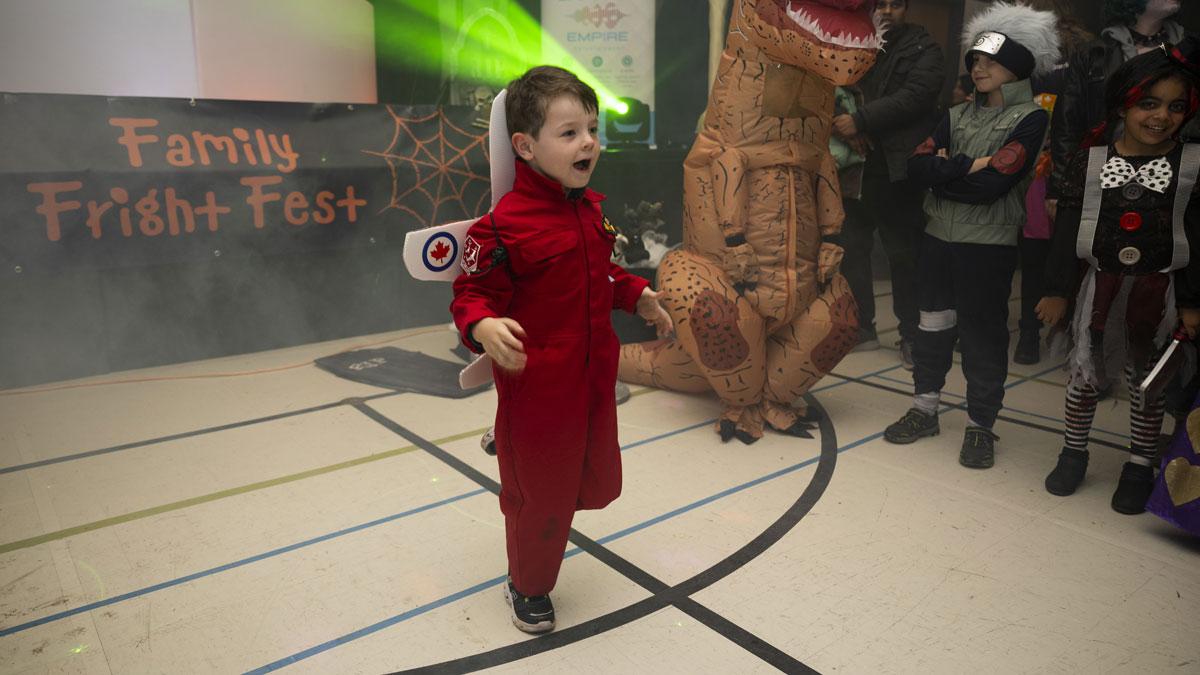 Child in a red astronaut costume excitedly participating in a Halloween event at "Family Fright Fest." Background includes other costumed individuals and festive decorations.