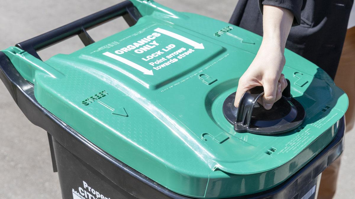 Person opening the lid of a green organic cart.