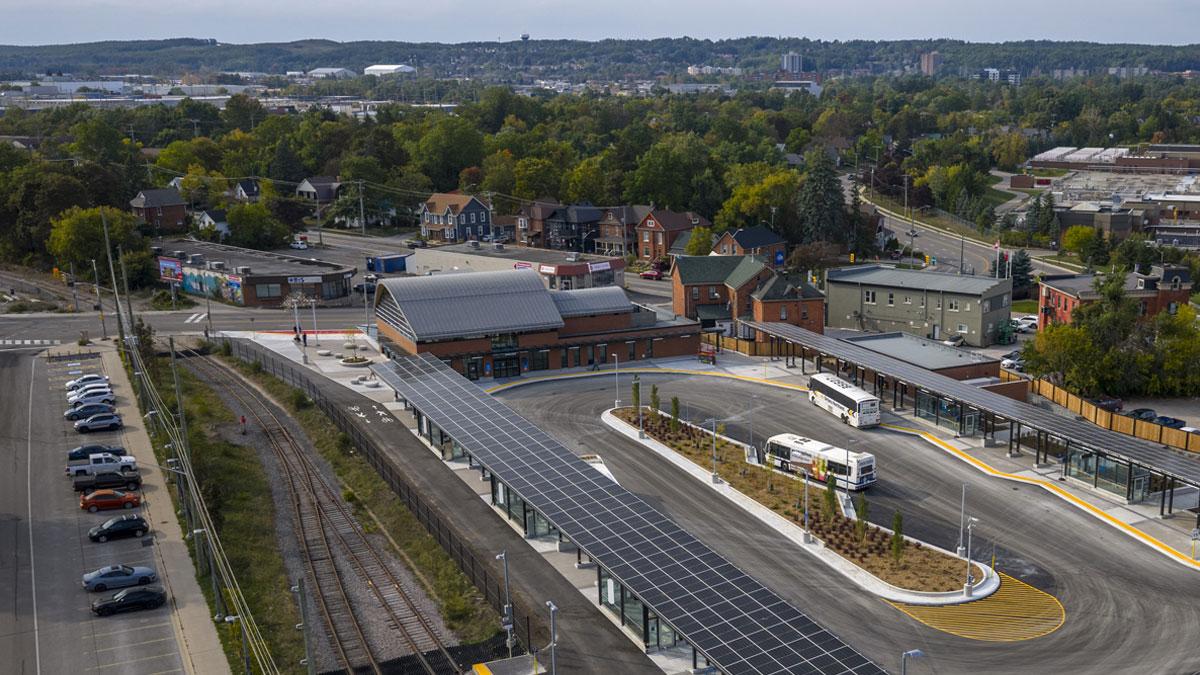 Aerial view of a bus terminal with solar panels, surrounded by trees and roads.