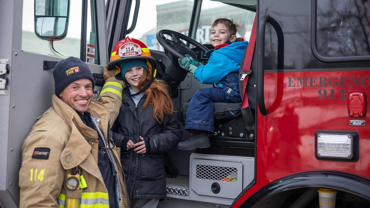 Firefighter with smiling children in a firetruck cab.
