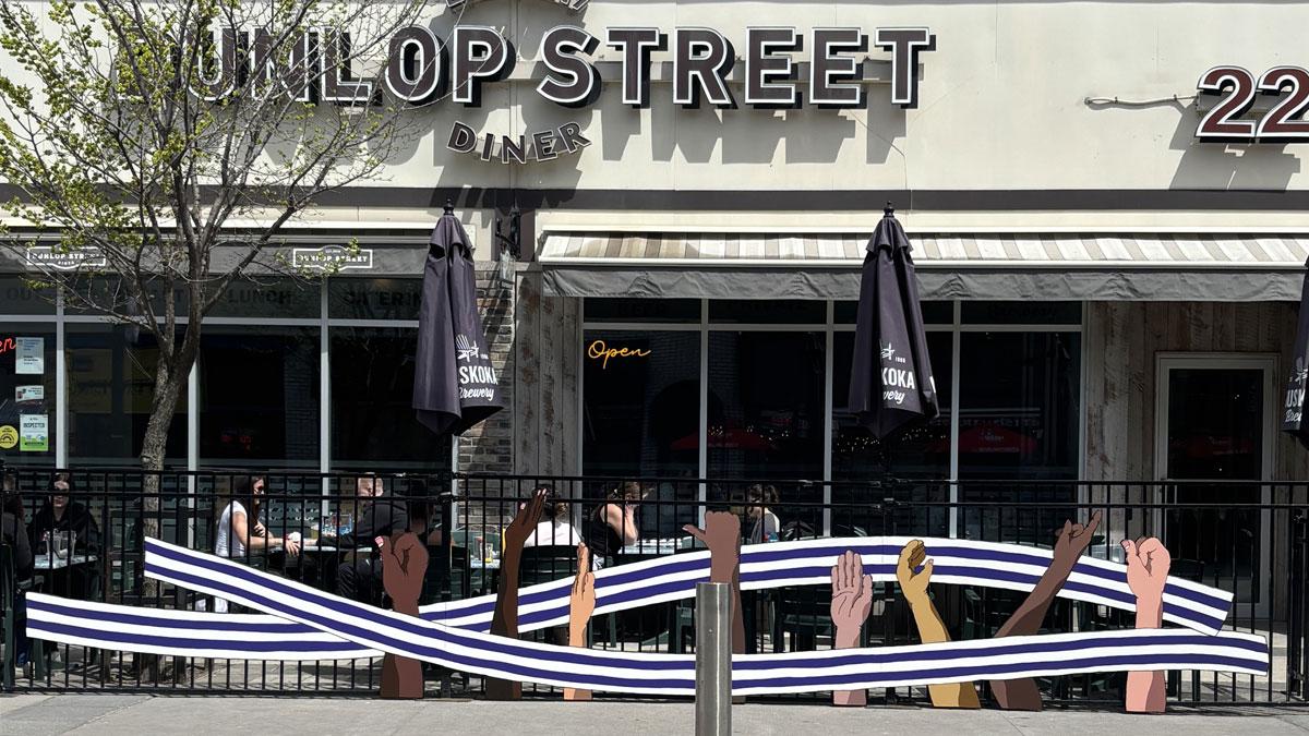 Restaurant with artwork on the patio fence of a white and purple belt runs and hands of different skin tones doing sign language.