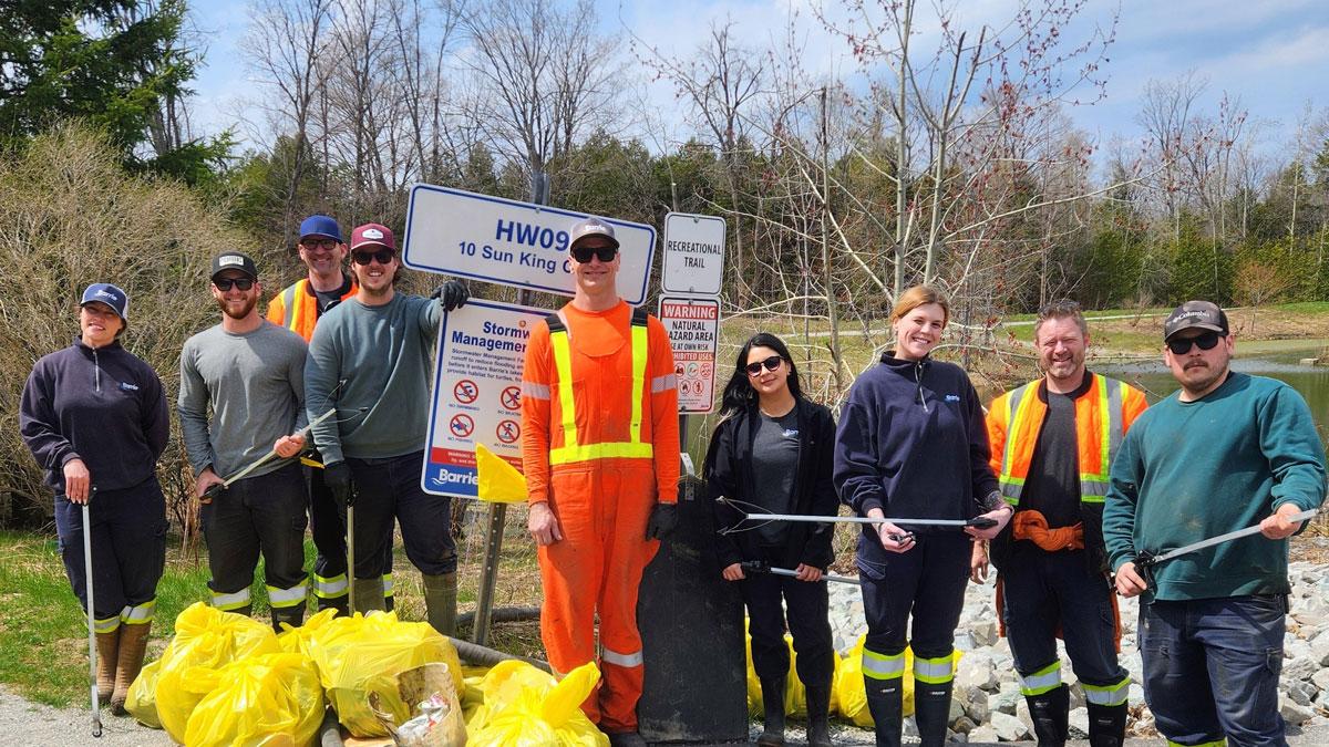 Group of volunteers in safety vests, posing with trash bags on a sunny day.