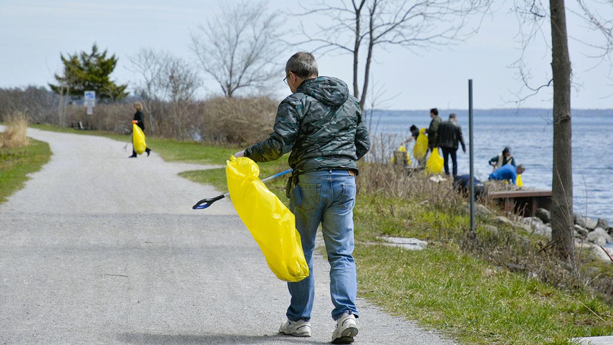 People cleaning up along a waterfront path, holding yellow garbage bags.