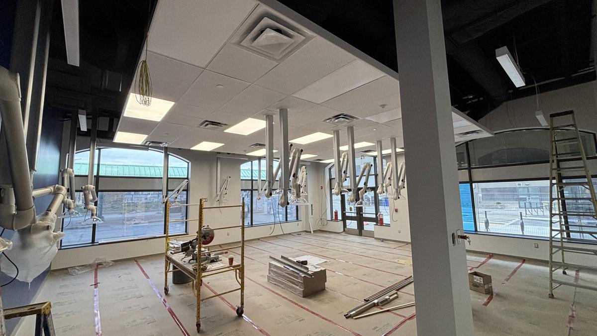 Interior of a partially constructed room with lab equipment hanging from the ceiling, scaffolding, and large windows.