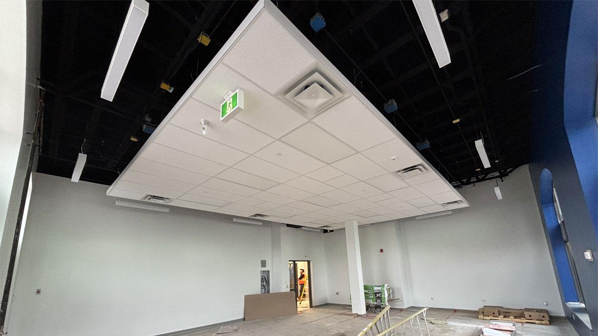 Empty room with a suspended ceiling, exposed framing, and construction materials visible.