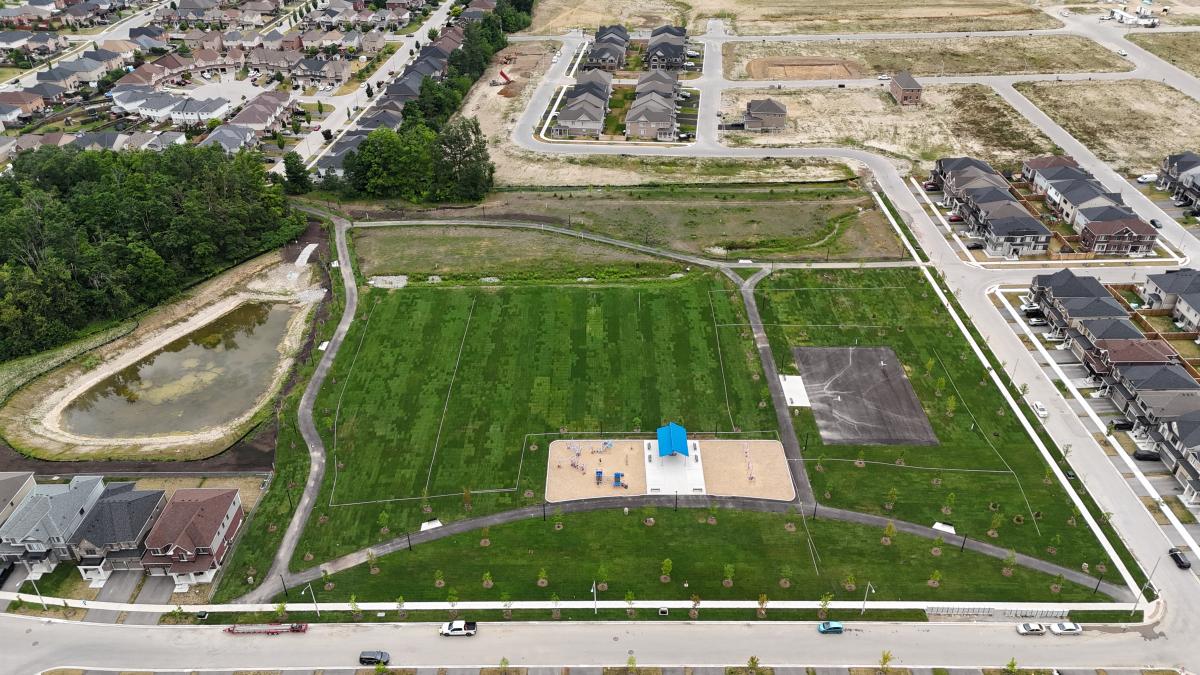 Aerial view of a green park with a playground, surrounded by newly developed homes and empty land.