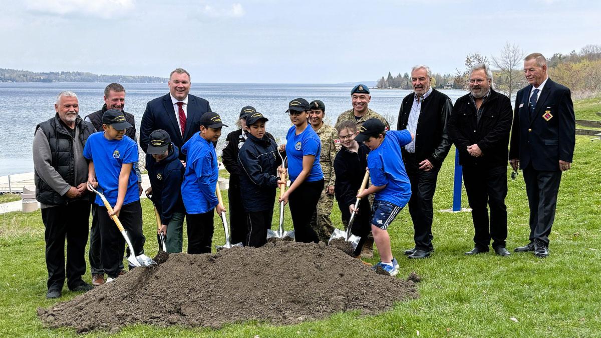 A group of children and adults participate in a groundbreaking ceremony by the waterfront.
