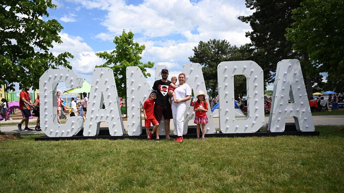 A group of five people in front of large, illuminated letters spelling "CANADA" on a grassy area.