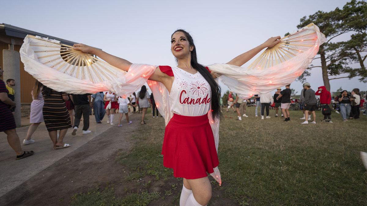 Dancer in a red skirt and white top poses holding illuminated fans at an outdoor event.