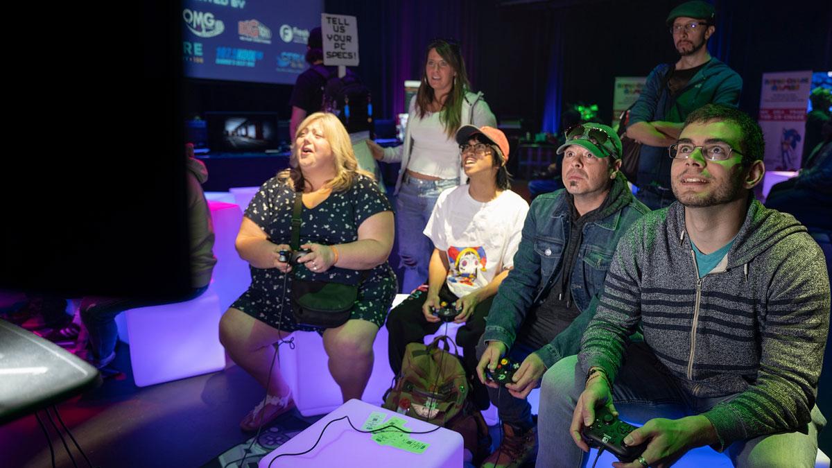A group of friends enjoying a video game session, smiling and engaged, in a colourful setting.