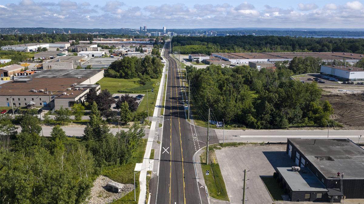 Aerial view of a long road lined with greenery, leading towards a distant city skyline.