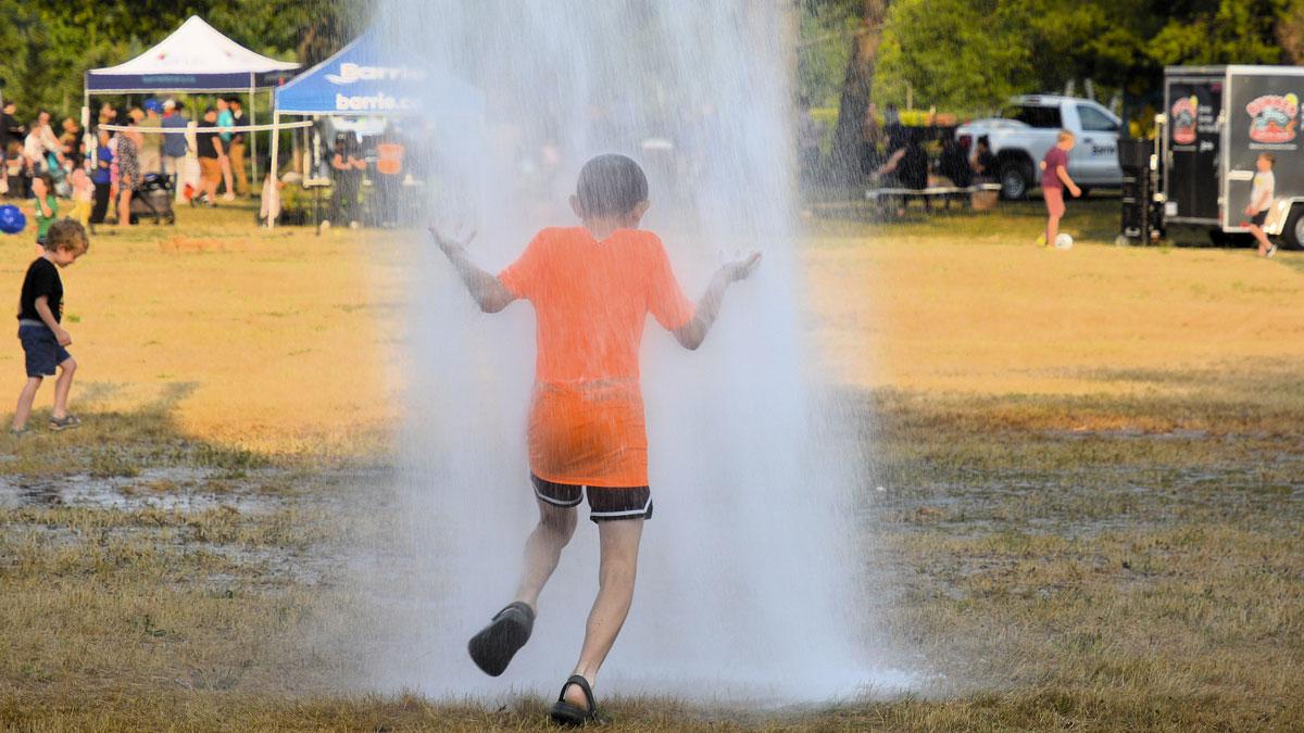 A child stands playfully under a water spray in a field.