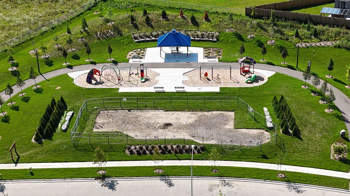 Aerial view of a park with playgrounds, a pavilion, pathways, and landscaped green areas.