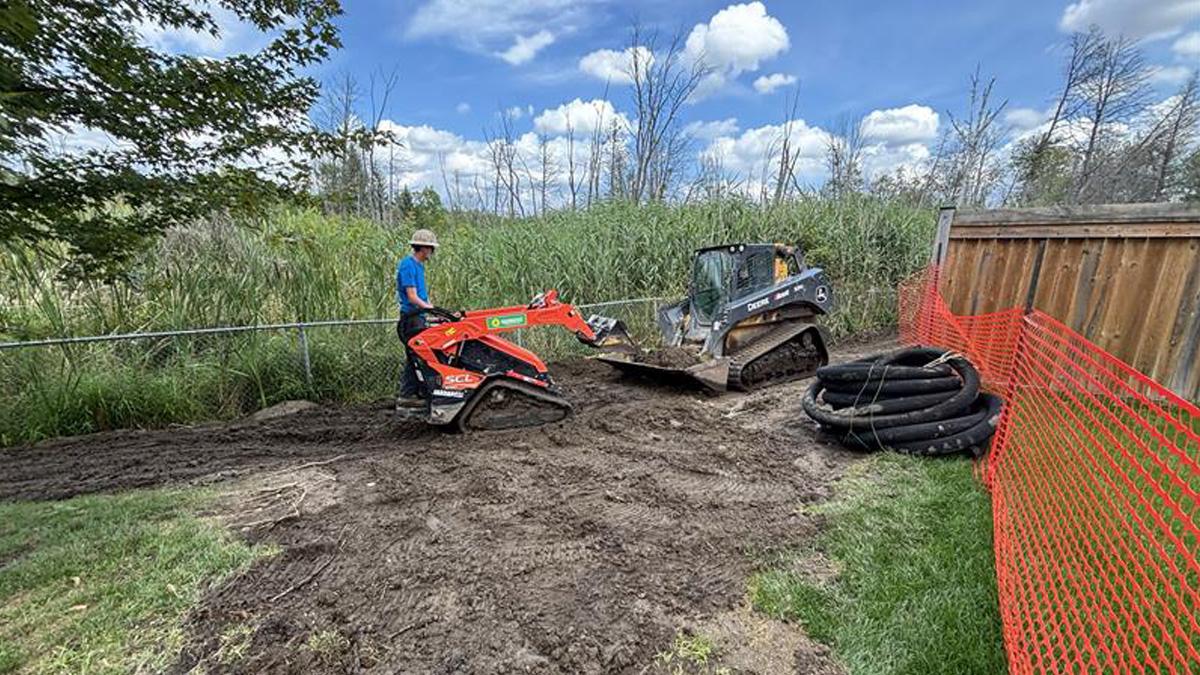 Construction workers operating machinery on a muddy site with orange safety fencing.