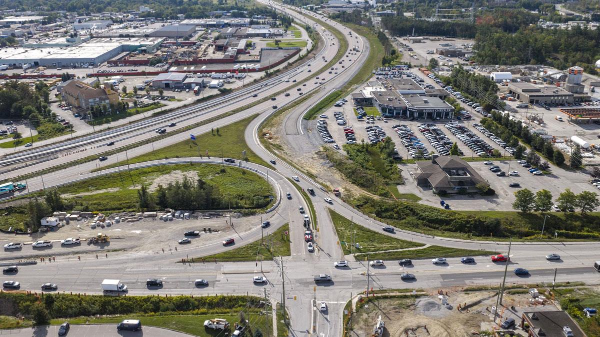 Aerial view of a busy highway intersection with vehicles, greenery, and commercial areas nearby.