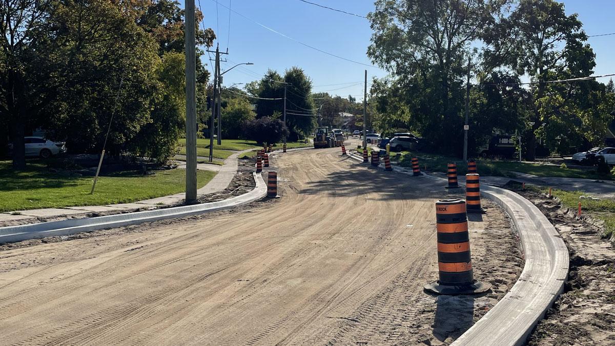 Construction site with a dirt road, orange safety cones, and workers in the background.
