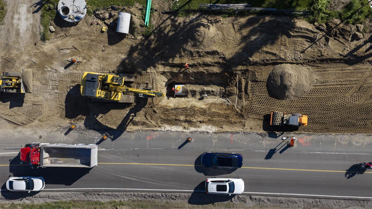 Construction site with heavy machinery, vehicles on the road, and freshly dug earth.