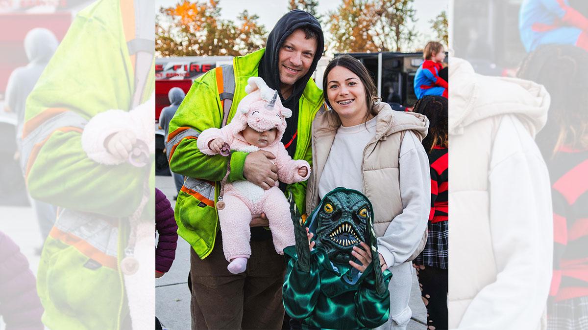 A family including smiling parents, a baby in a unicorn costume and a child in a reptilian costume.