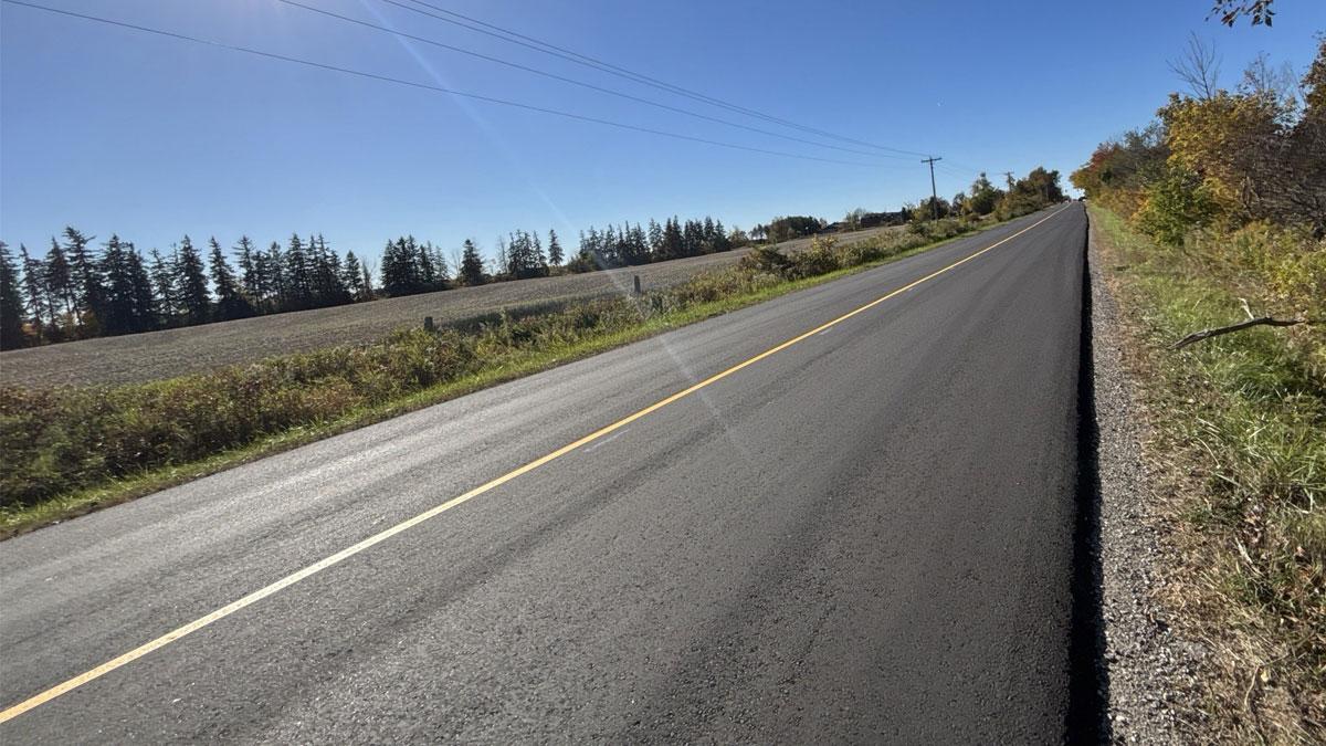 A freshly paved rural road lined with trees and fields.