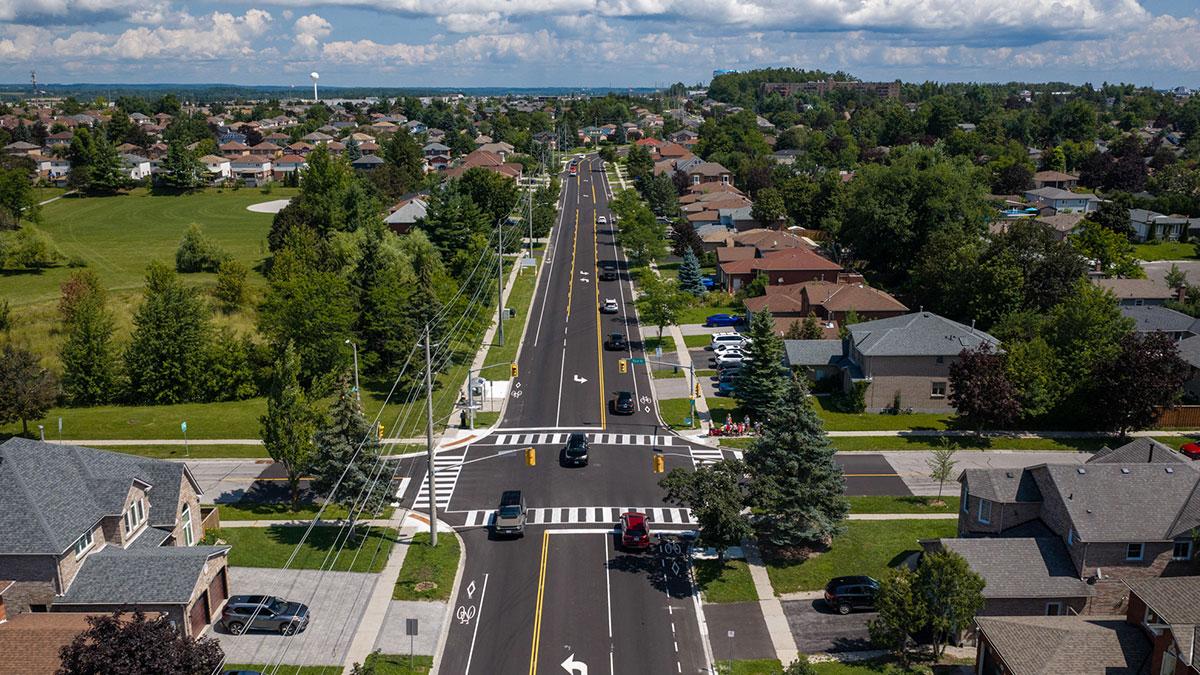 Aerial view of a freshly paved suburban street with line markings, lined with houses and trees.
