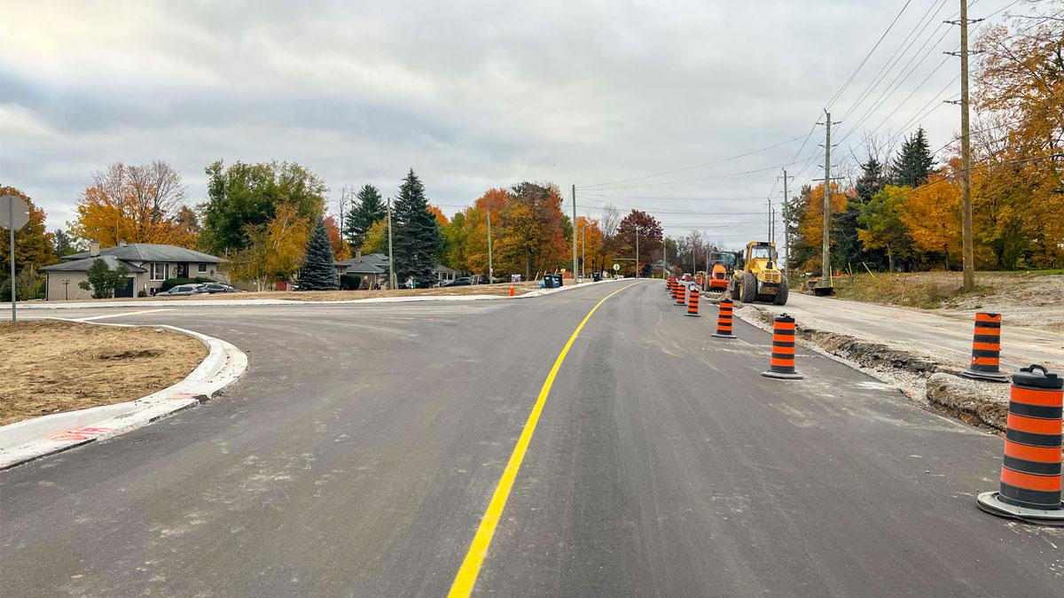 Construction site featuring a newly paved road with yellow markings and orange traffic cones.