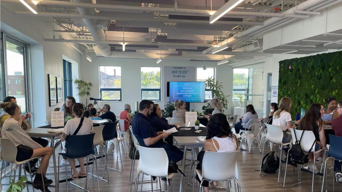 A modern workspace with people engaged in discussions, featuring greenery and a presentation screen.