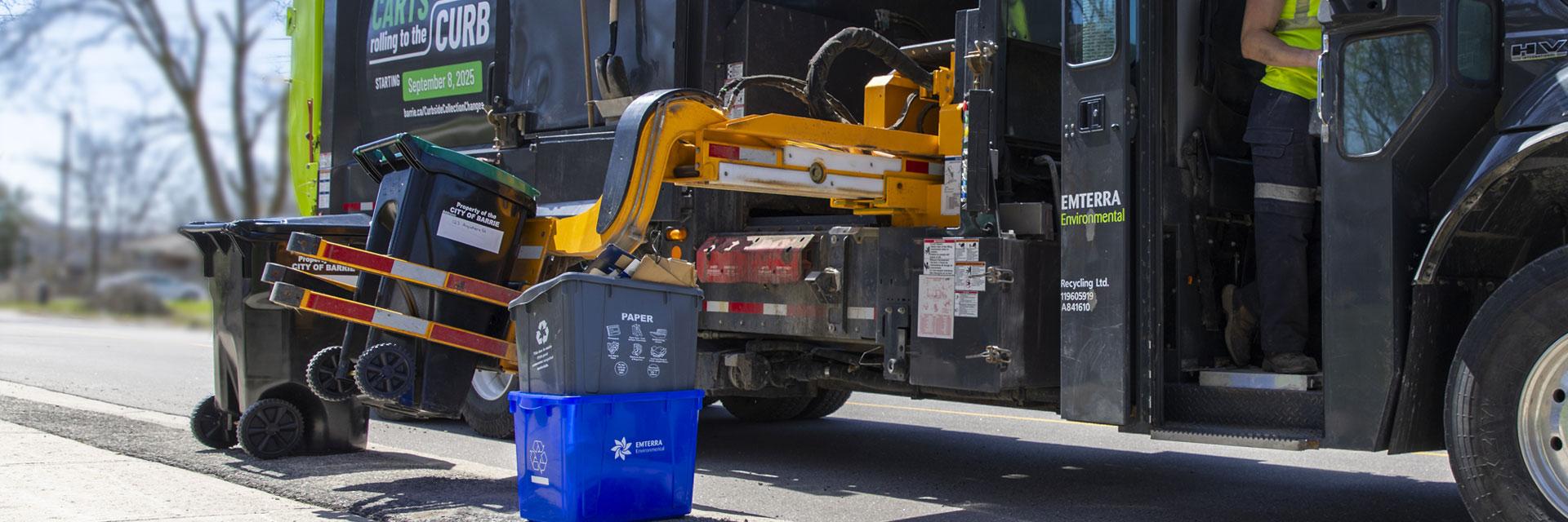 A Waste Management truck collects an organics cart from the curb, assisted by a worker in high visibility clothing.