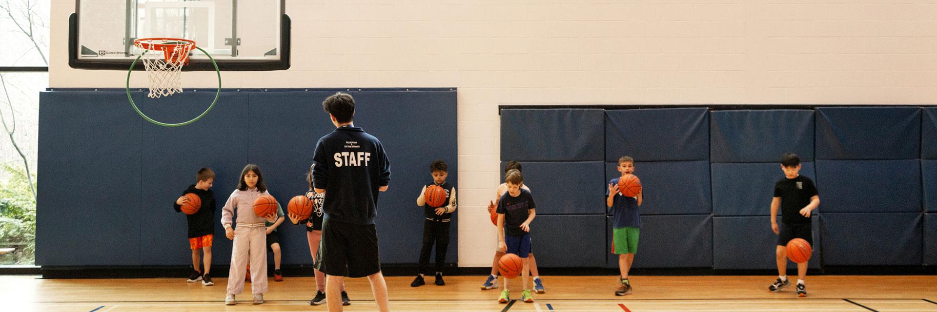 Basketball coach instructs young players in a gym, each holding a basketball.