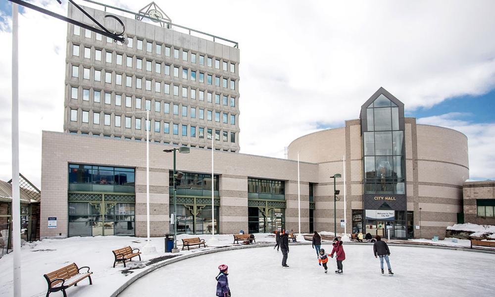 Skaters on circular ice rink with City Hall building in background