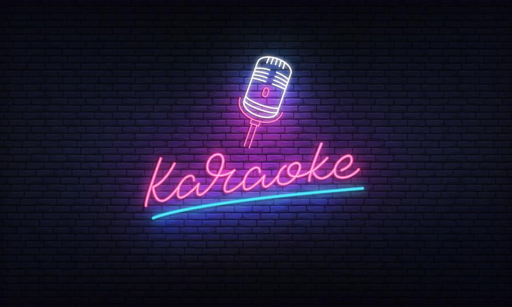 Neon pink and blue text "Karaoke" and mic icon on brick wall 